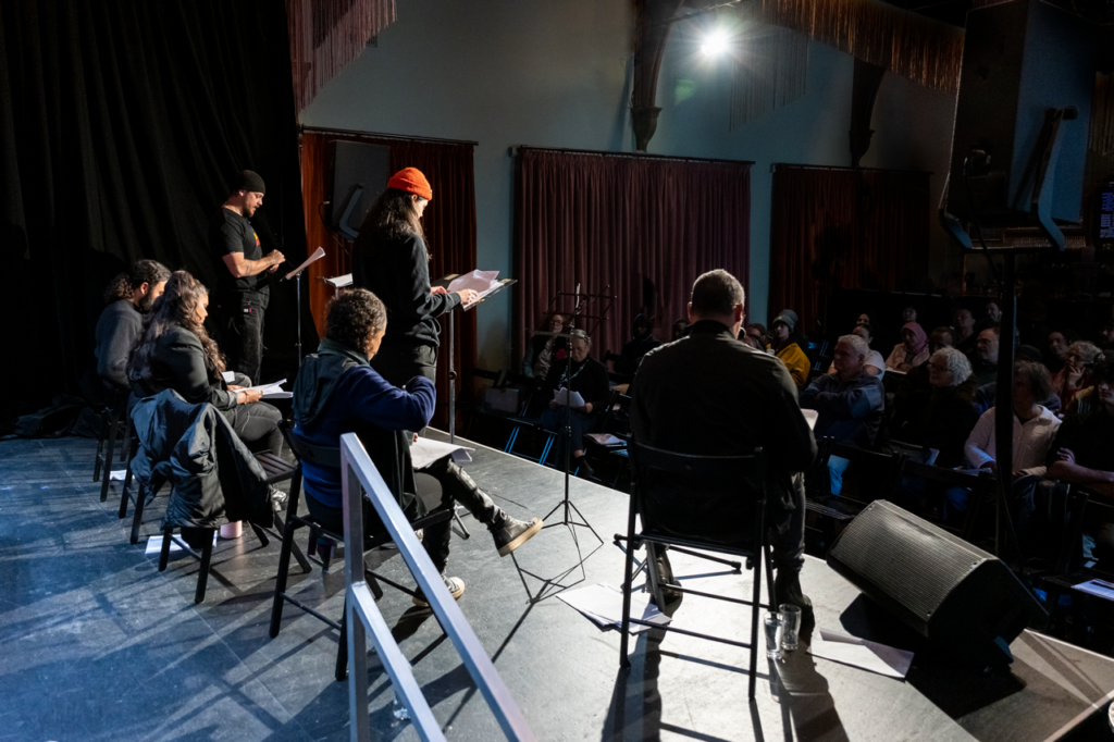 back of stage view towards audience. five people on stage reading scripts.